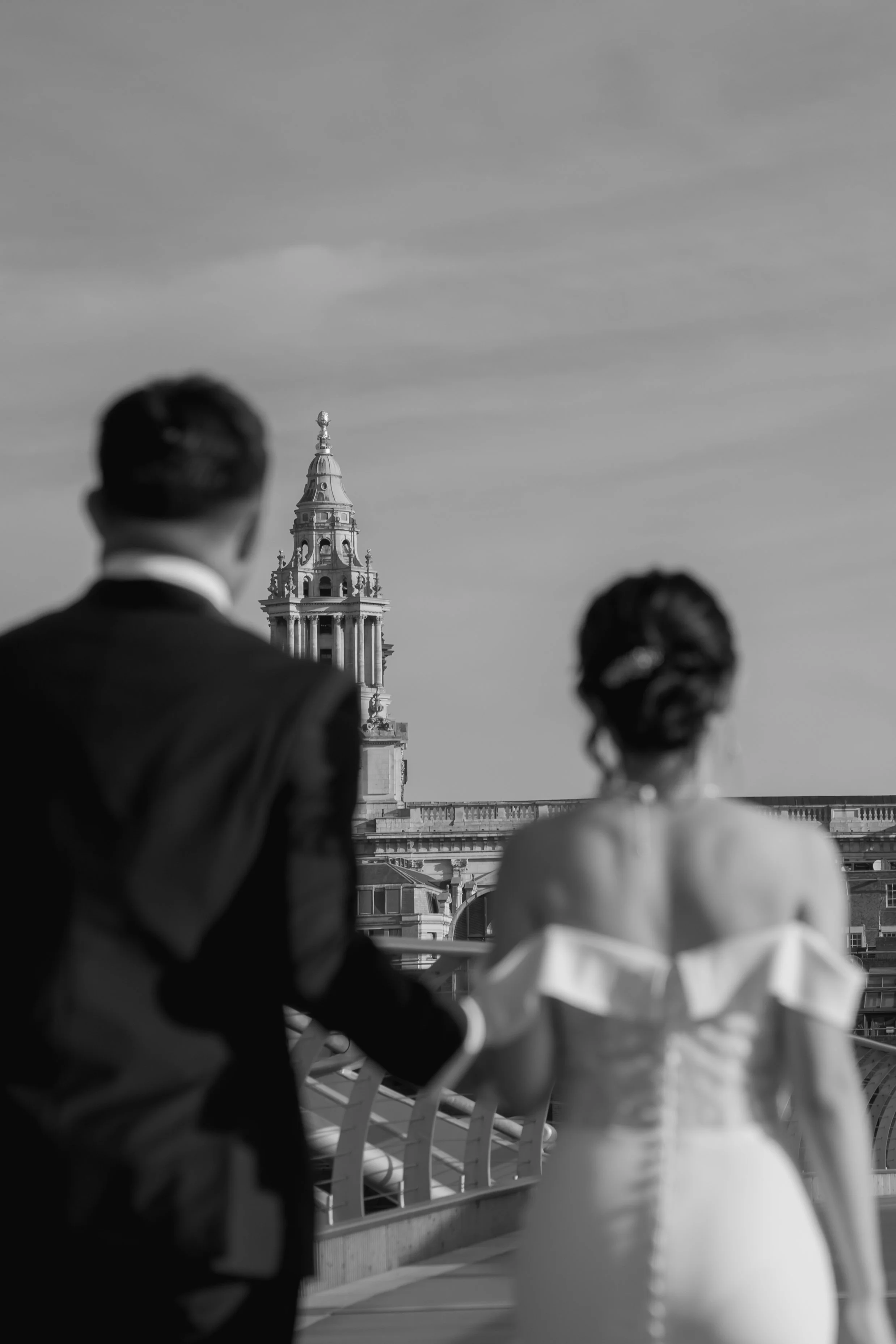 結婚式の新郎と新婦が屋上で手をつなぎながら立っている写真。背景には古典建築の塔が見える。