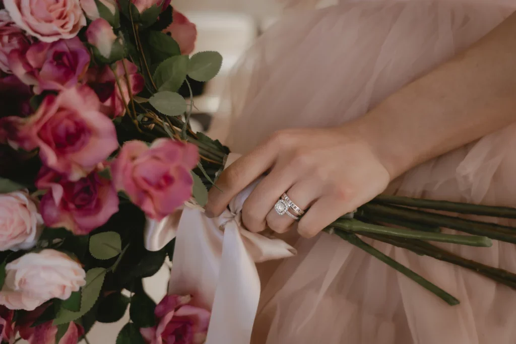 ピンクのバラとホワイトのバラの花束と、ダイヤモンドの結婚指輪と婚約指輪をつけた女性の手が写っている