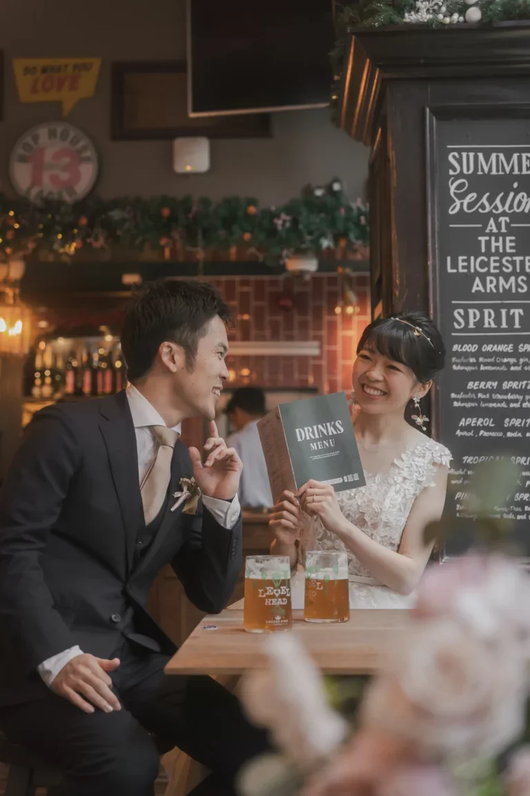 バーで笑顔の恋人たちがドリンクを持ちながら会話している。