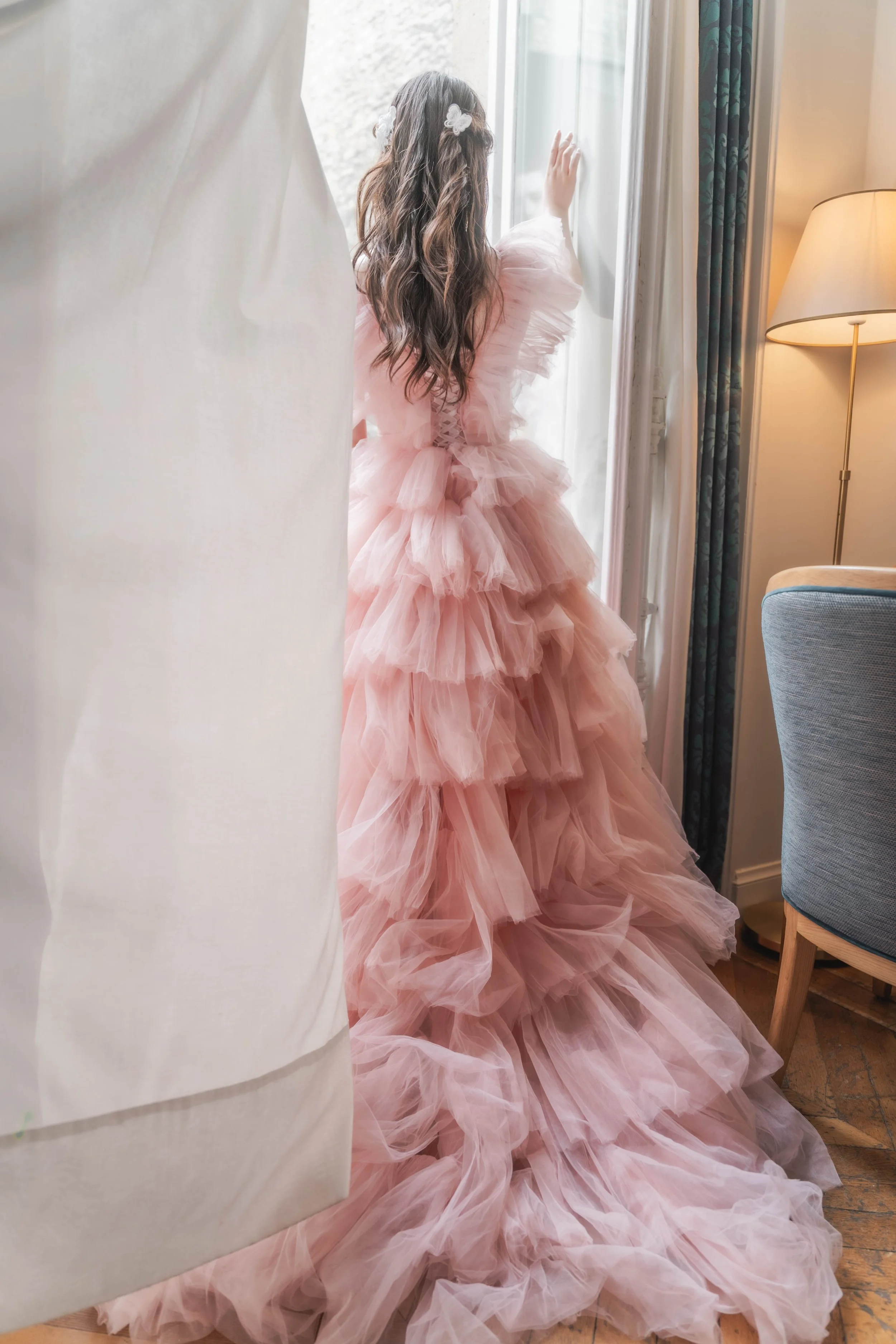 ピンクのドレスを着た少女が窓のそばで外を見ている