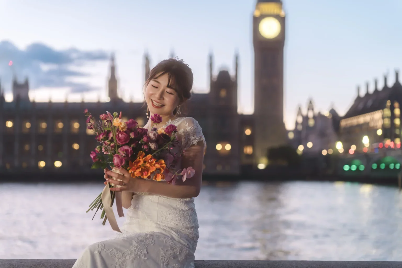 夕暮れ時のロンドンの川辺で、笑顔の女性が花束を持っている