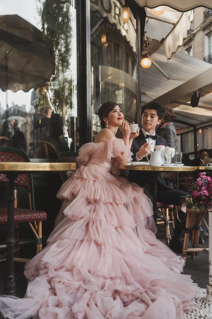 結婚式のようなフォーマルな場でピンクのドレスを着た新婦と紺の燕尾服を着た新郎がお茶を楽しんでいる。