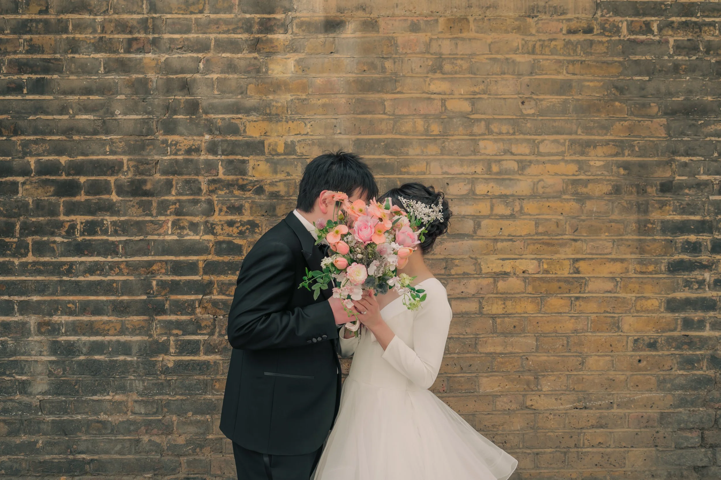 結婚式の衣装を着た男女が花束を持ちながら壁に寄り添っている写真