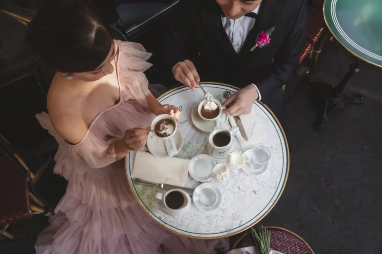 女性と男性がお茶を飲みながら会話しているテーブルの上に、コーヒーやティースプーンなどの小さな皿やカップが置かれている。