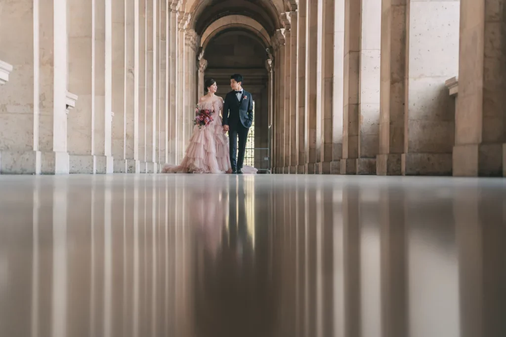 結婚式のドレスとスーツを着たカップルが柱の並ぶ建物の廊下を歩いている