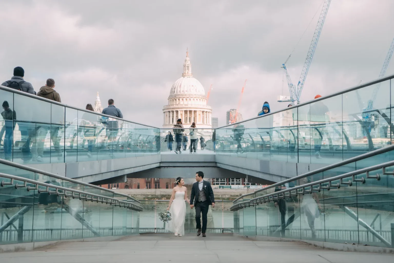 結婚式のカップルが歩いているロンドンのテムズ川沿いの歩道。背景にセント・ポール大聖堂と建設中のクレーンが見える。