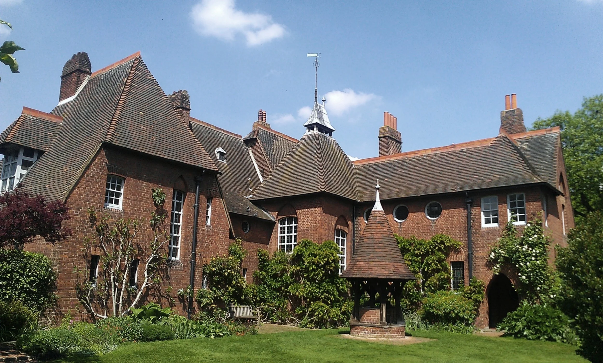 A 19C red brick Design Reform house, considered Arts and Crafts, consisting of several conjoined volumes, inspired by Medieval manor houses