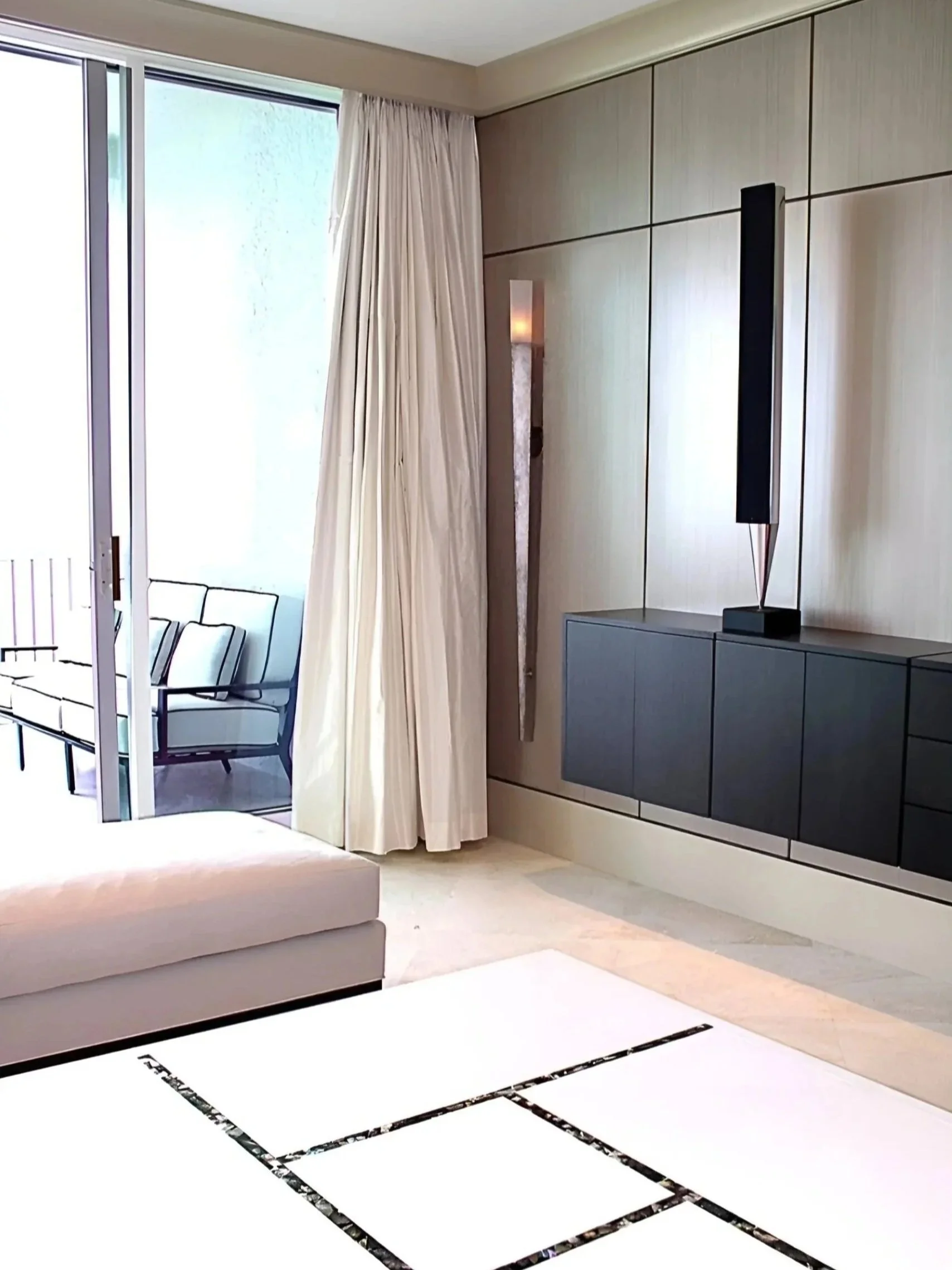 Detail of an apartment living room corner with draper, sconce, speaker, partial coffee table and chaise, view of porch