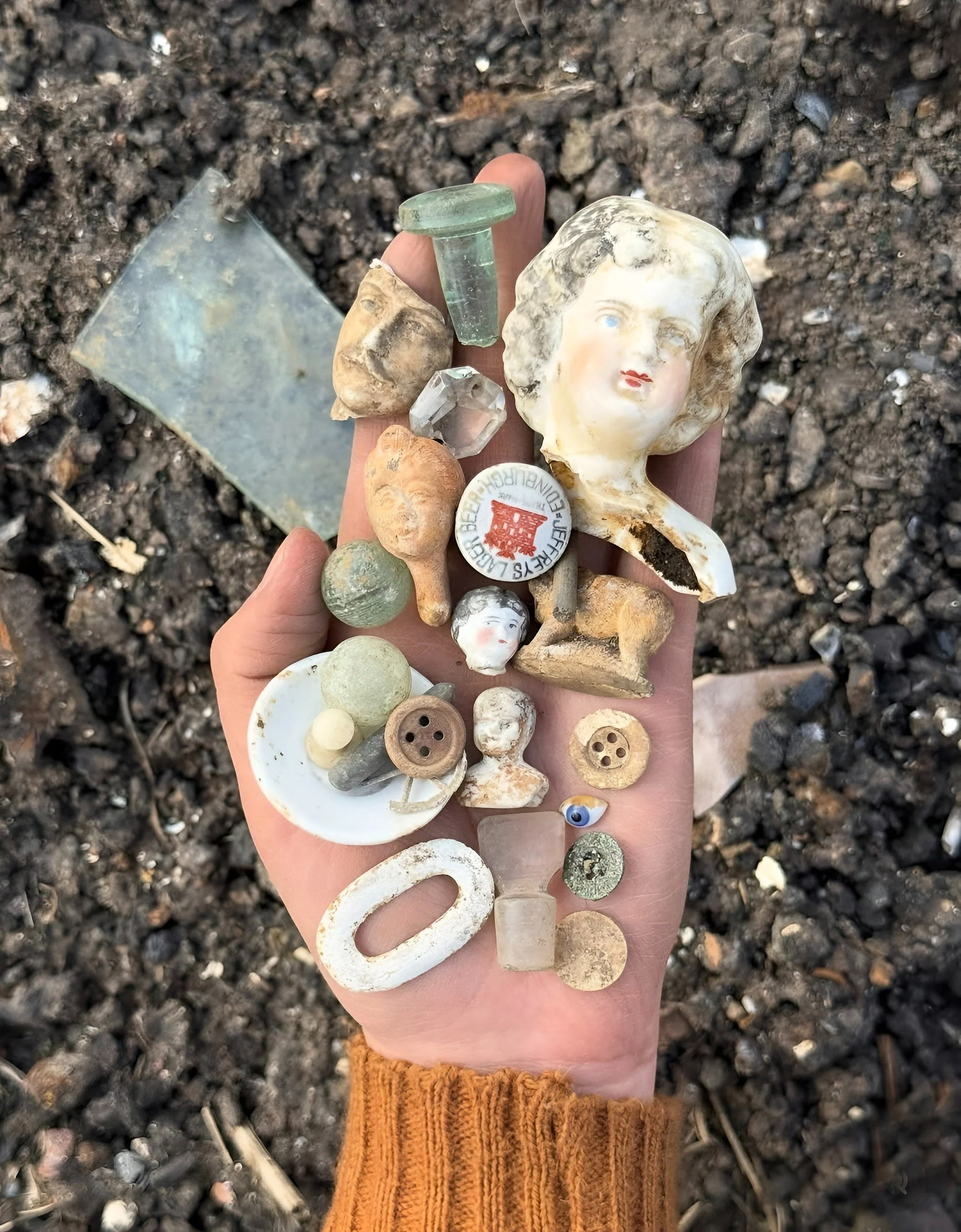 Assorted found objects including pottery fragments, glass, and small artifacts held in a person’s hand