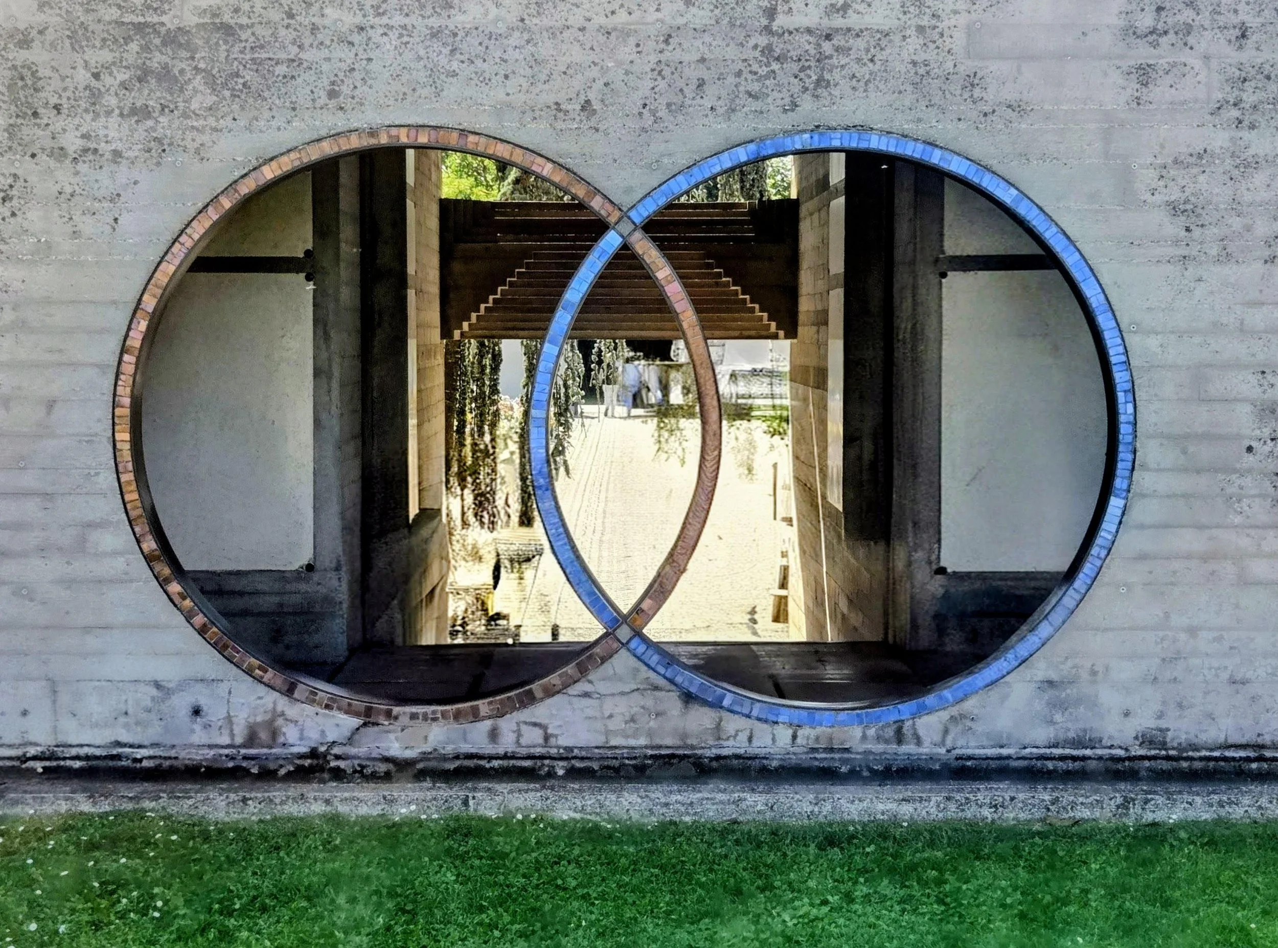 Two large intersecting open circles in a concrete wall trimmed with bronze and blue glass tile