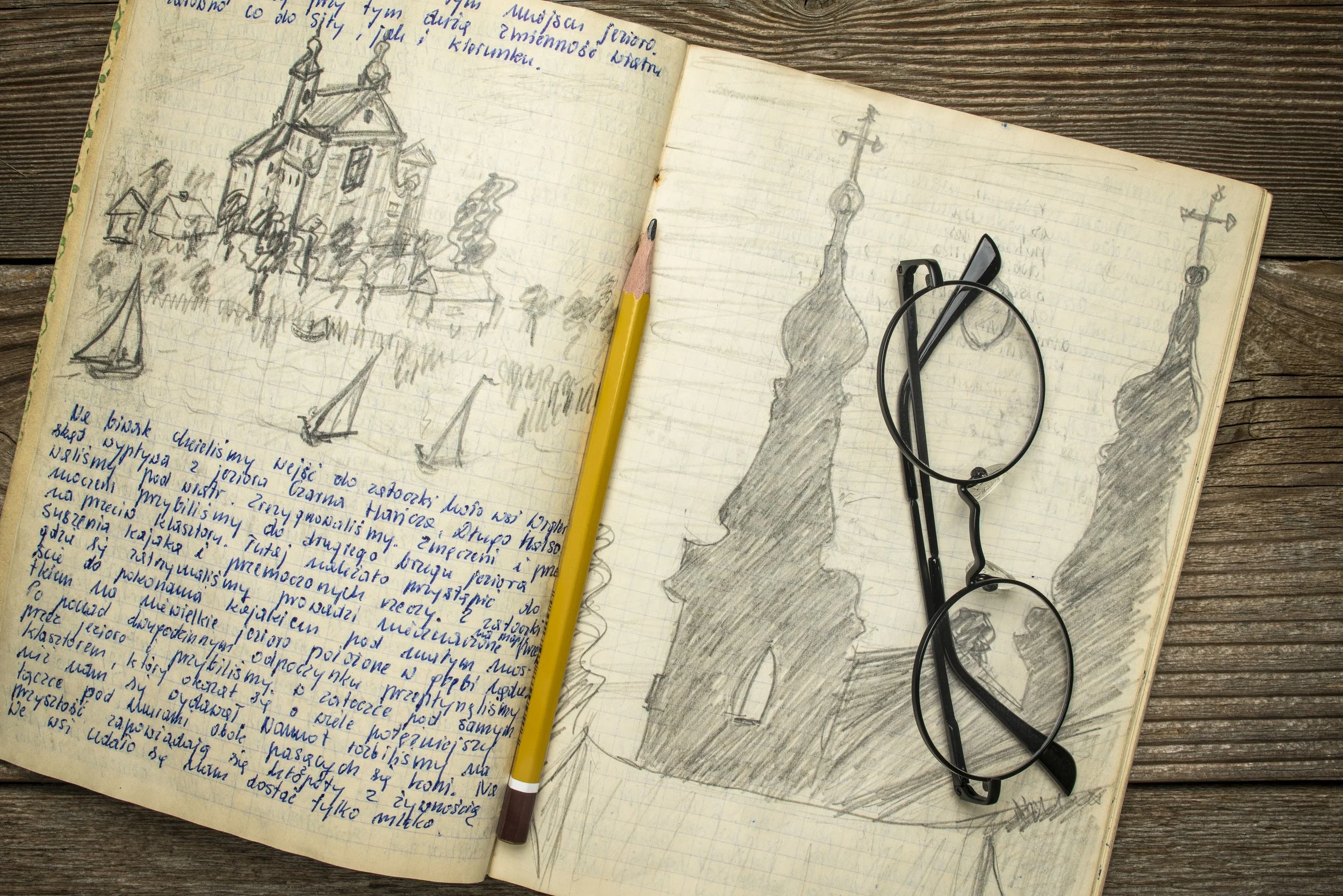 An open notebook with pencil and glasses showing writing and sketches
