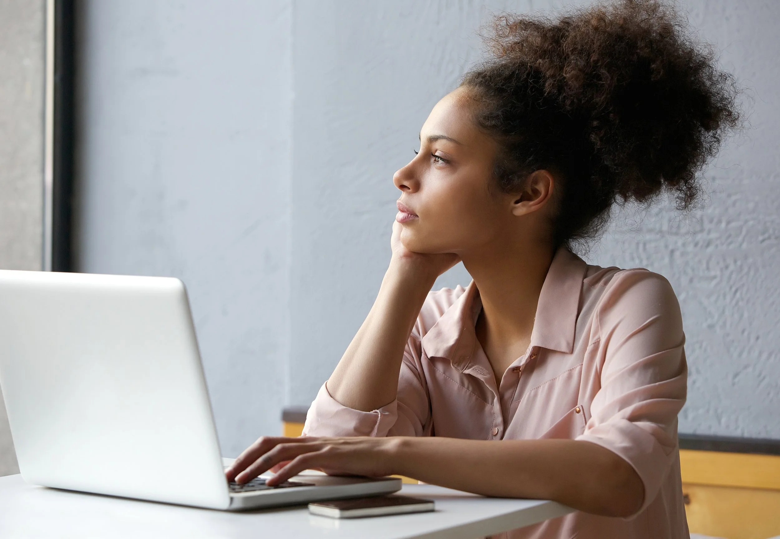 A young girl at a laptop who has stopped work and is daydreaming