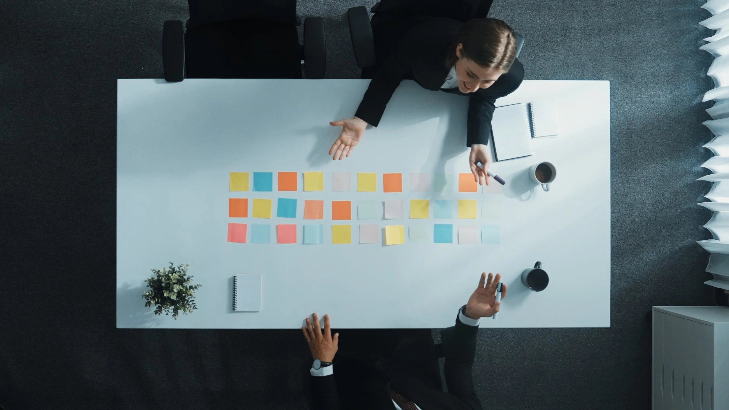 2 business people on opposite sides of a table discussing a grid on the table made from different colored stickies
