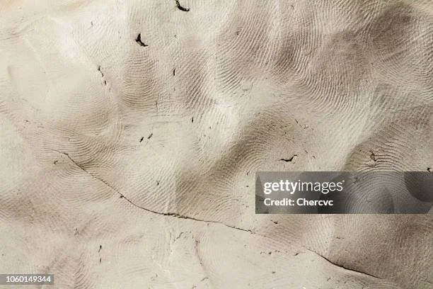 Close-up of textured sand with footprints and a thin curved line.
