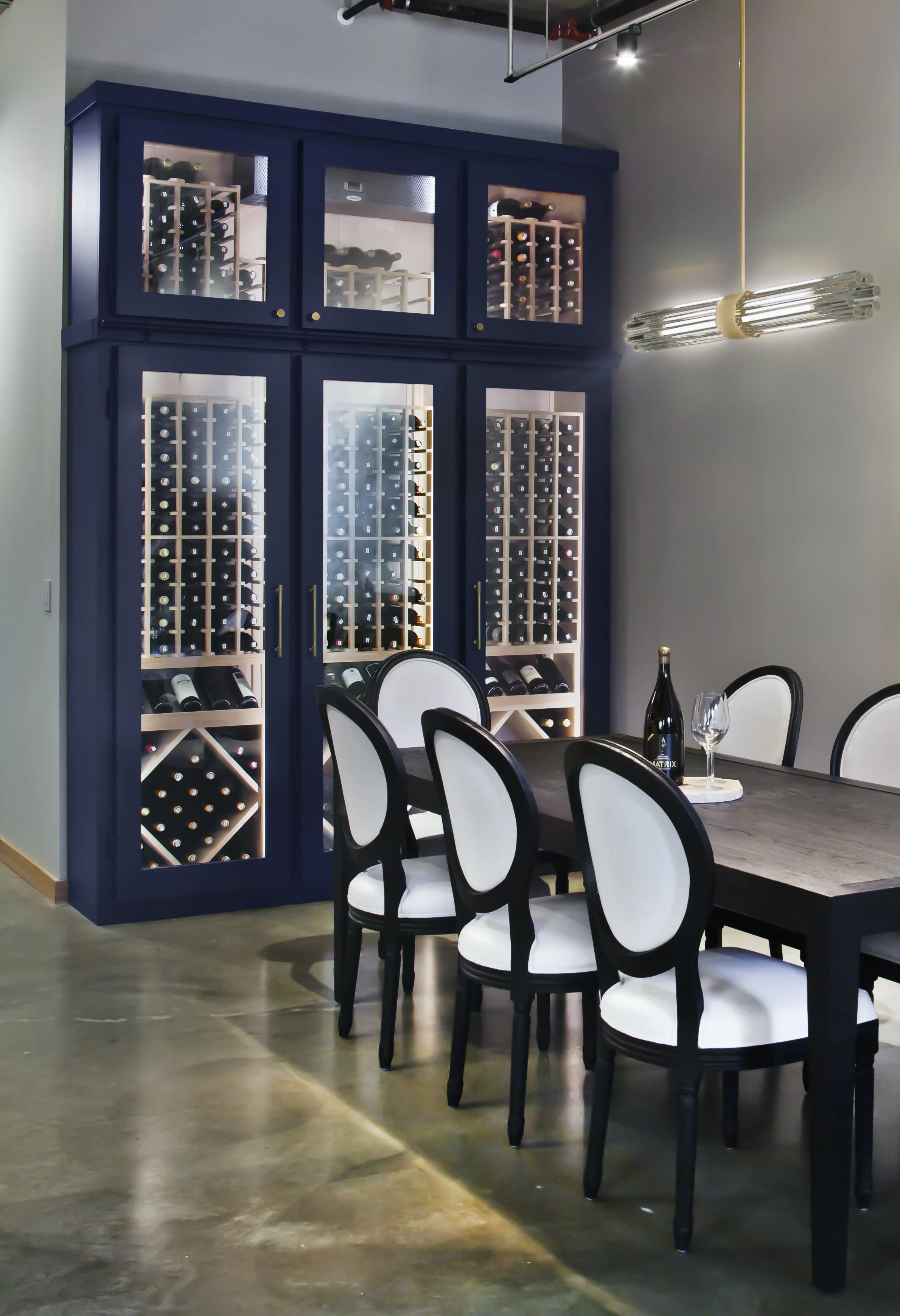 A dining room with a large blue wine cabinet filled with wine bottles and a dark wooden dining table with white upholstered chairs.