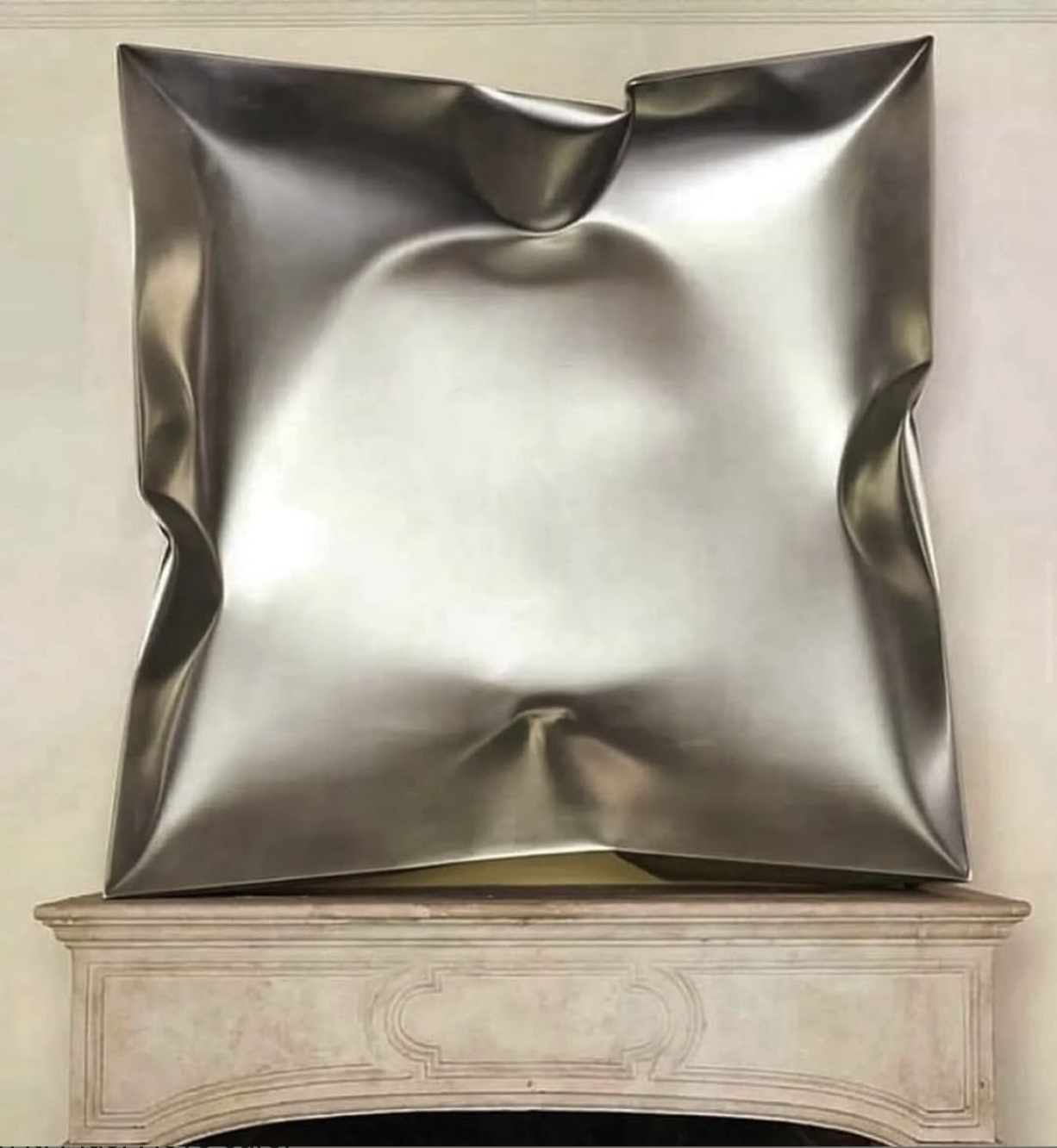 A crumpled metallic square modern sculpture placed on a fireplace mantel.