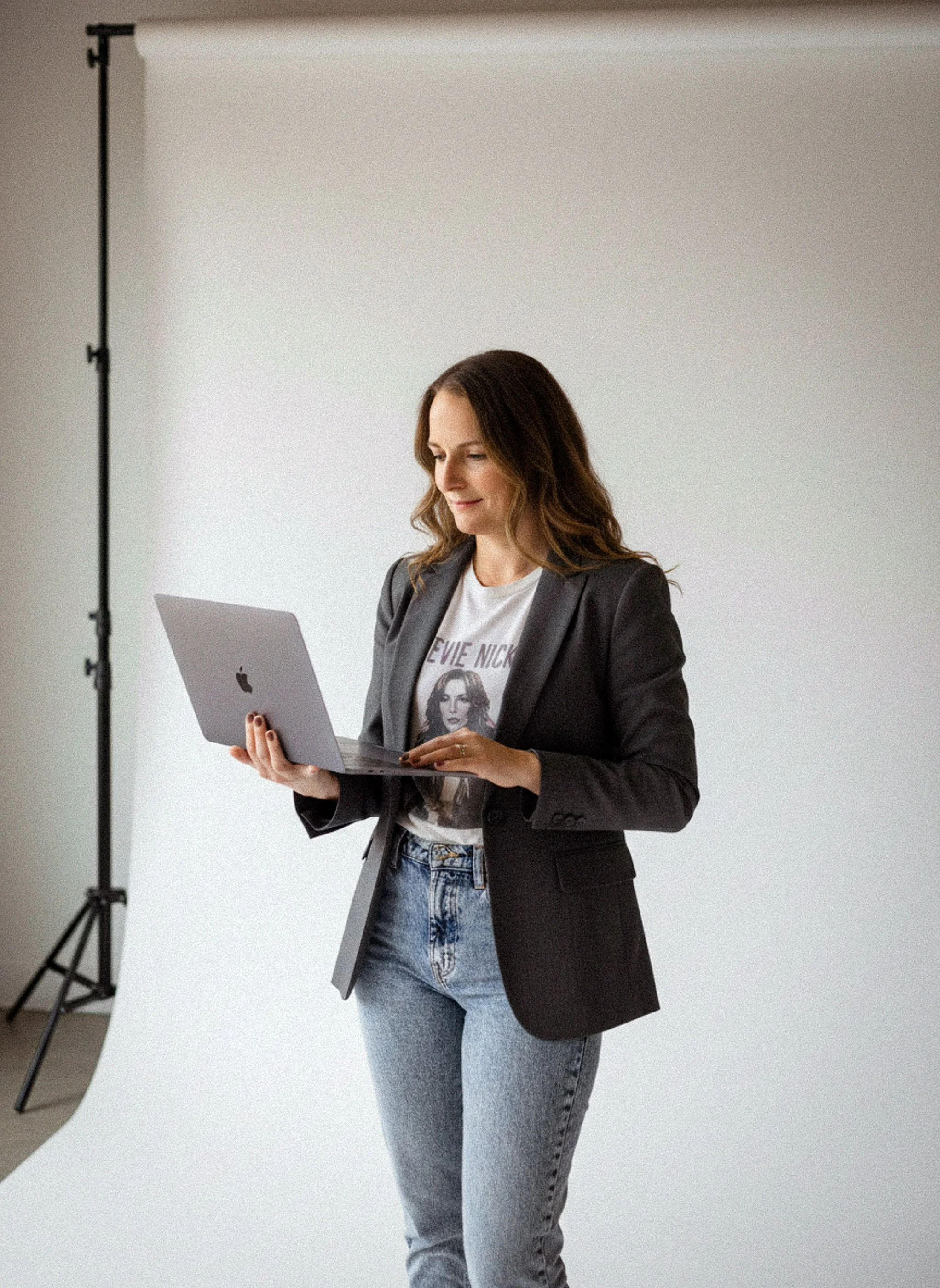 Liz founder of Aviso Studios, a Santa Cruz-based website designer and strategist, standing with an open laptop in a clean, minimal studio — looking focused and approachable.