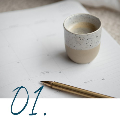 A cup of coffee or tea, a gold pen, and an open planner or calendar on a table.