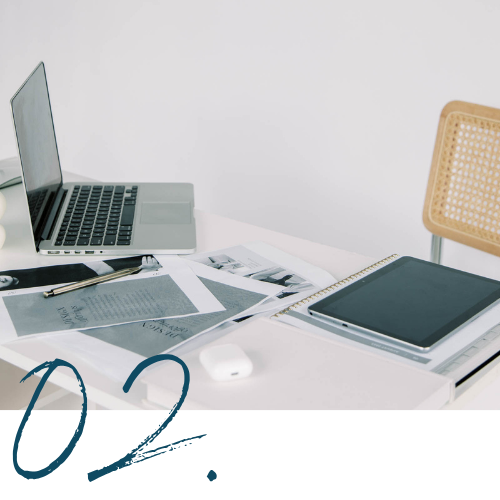 Work desk with a laptop, digital tablet, papers, and a mouse on a white surface in a clean, minimalistic setting.