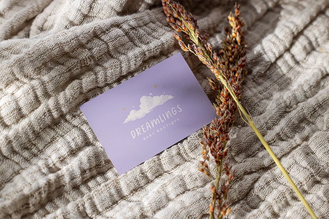 Dreamlings baby boutique business card mockup placed on textured fabric with dried florals, showcasing soft pastel branding.