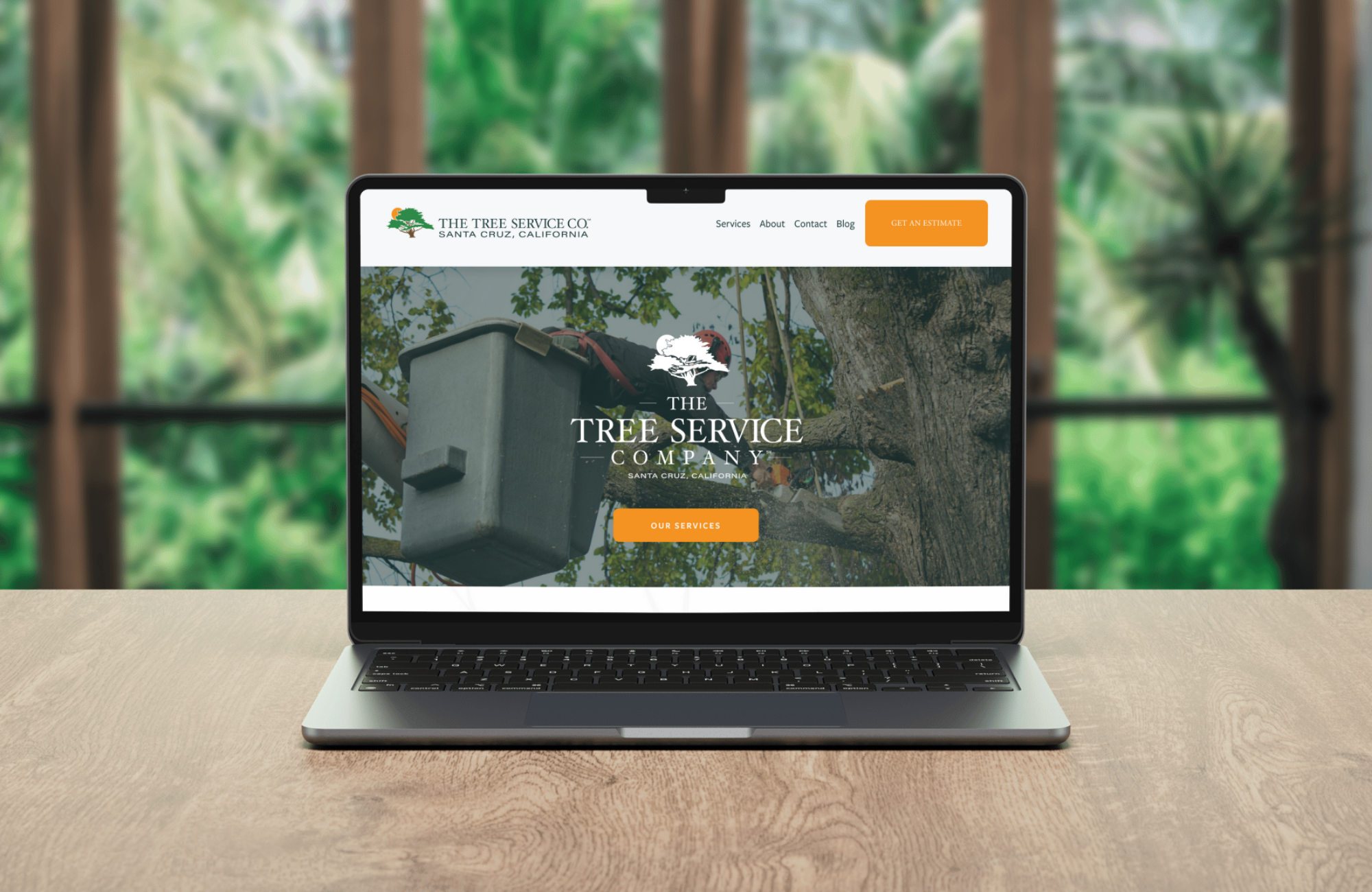 Laptop on a wooden table displaying the website design of The Tree Service Company, with a background of a tree branch, leaves, and a green outdoor setting.
