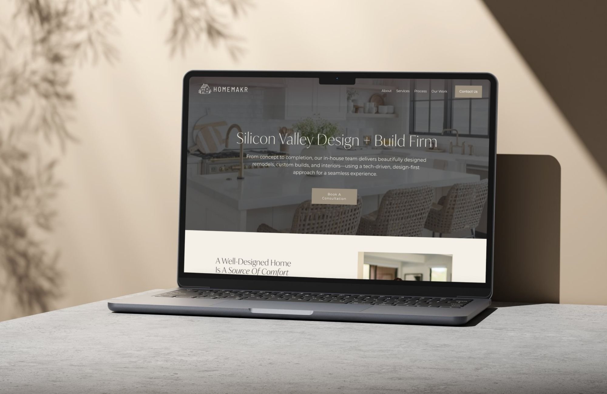 Laptop on a table displaying a home design and build firm's website titled Silicon Valley Design + Build Firm, with a button to book a consultation.