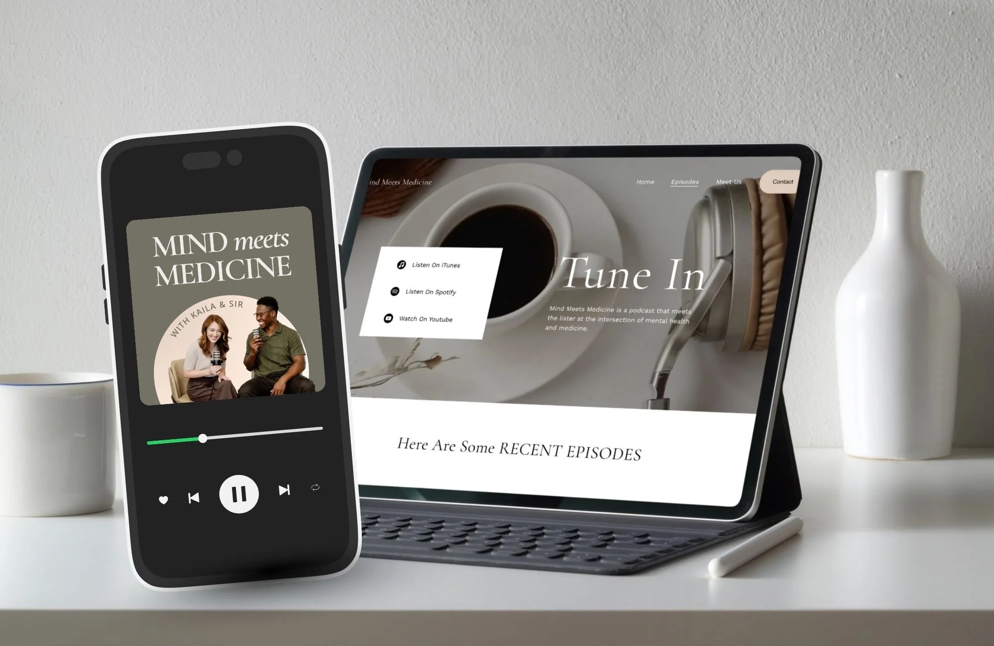 Smartphone and tablet on a white desk displaying a mental health podcast called 'Mind Meets Medicine,' with a coffee cup and a white vase nearby.