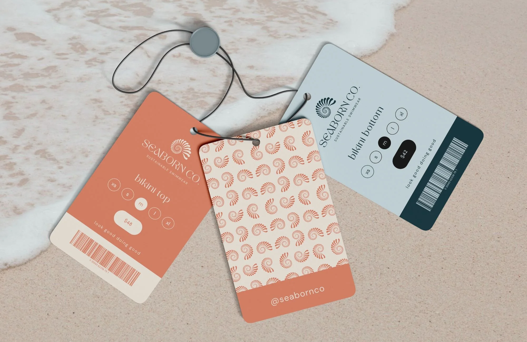 Tags from Seaborn Co. swimwear on sandy beach, one for a bikini top and one for a bikini bottom, with a patterned card in the middle and a barcode.