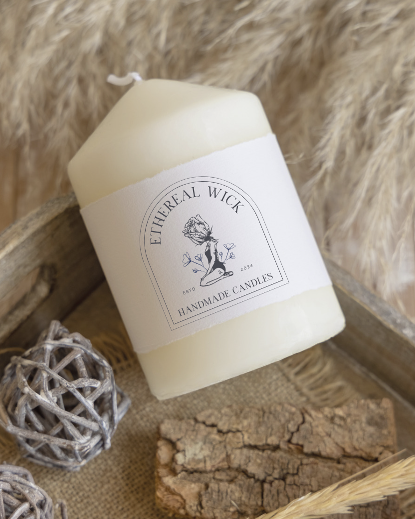 A white handmade candle with a label reading 'Etherial Wick Handmade Candles' placed inside a wooden box with decorative items like woven balls, bark, and dried grass around it.