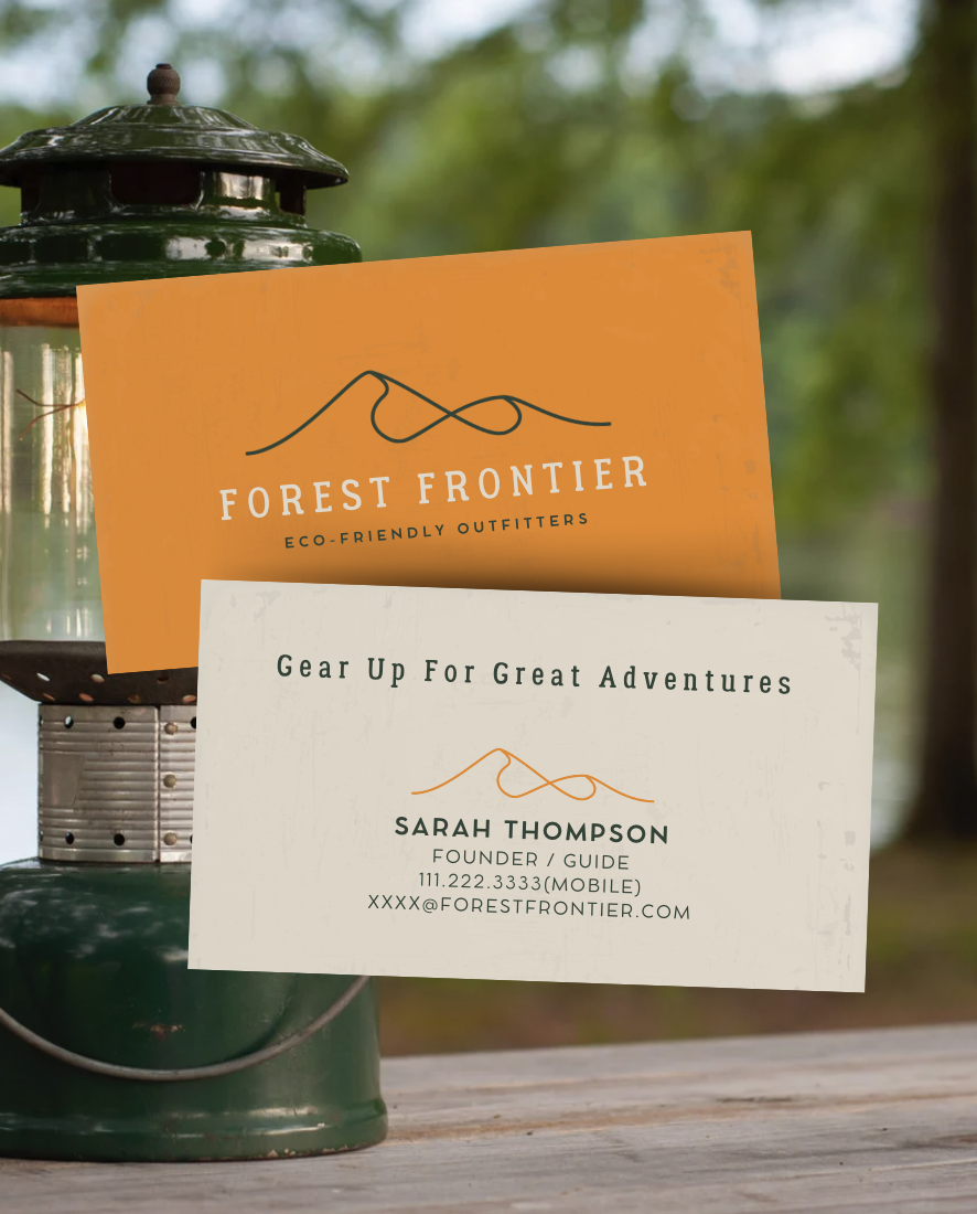 Business cards on a picnic table next to a green lantern in a forest setting. The orange card reads "Forest Frontier Eco-Friendly Outfitters" and the white card says "Gear Up For Great Adventures" with contact information for Sarah Thompson.