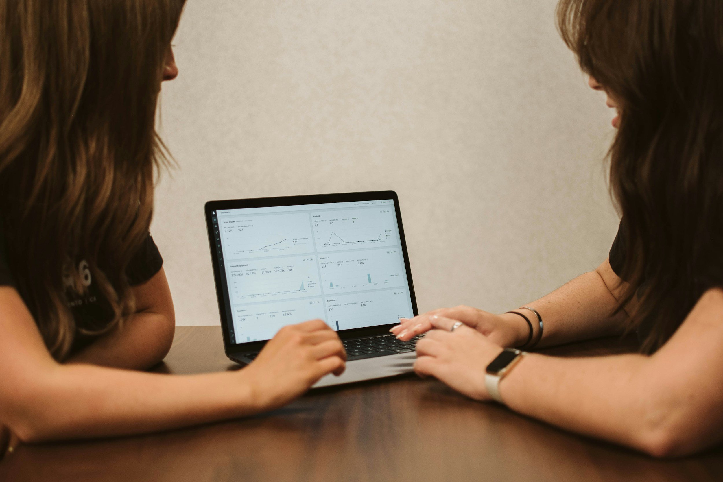 Two women sitting at a table looking at a laptop displaying website analytics and data graphs for a small business seo strategy