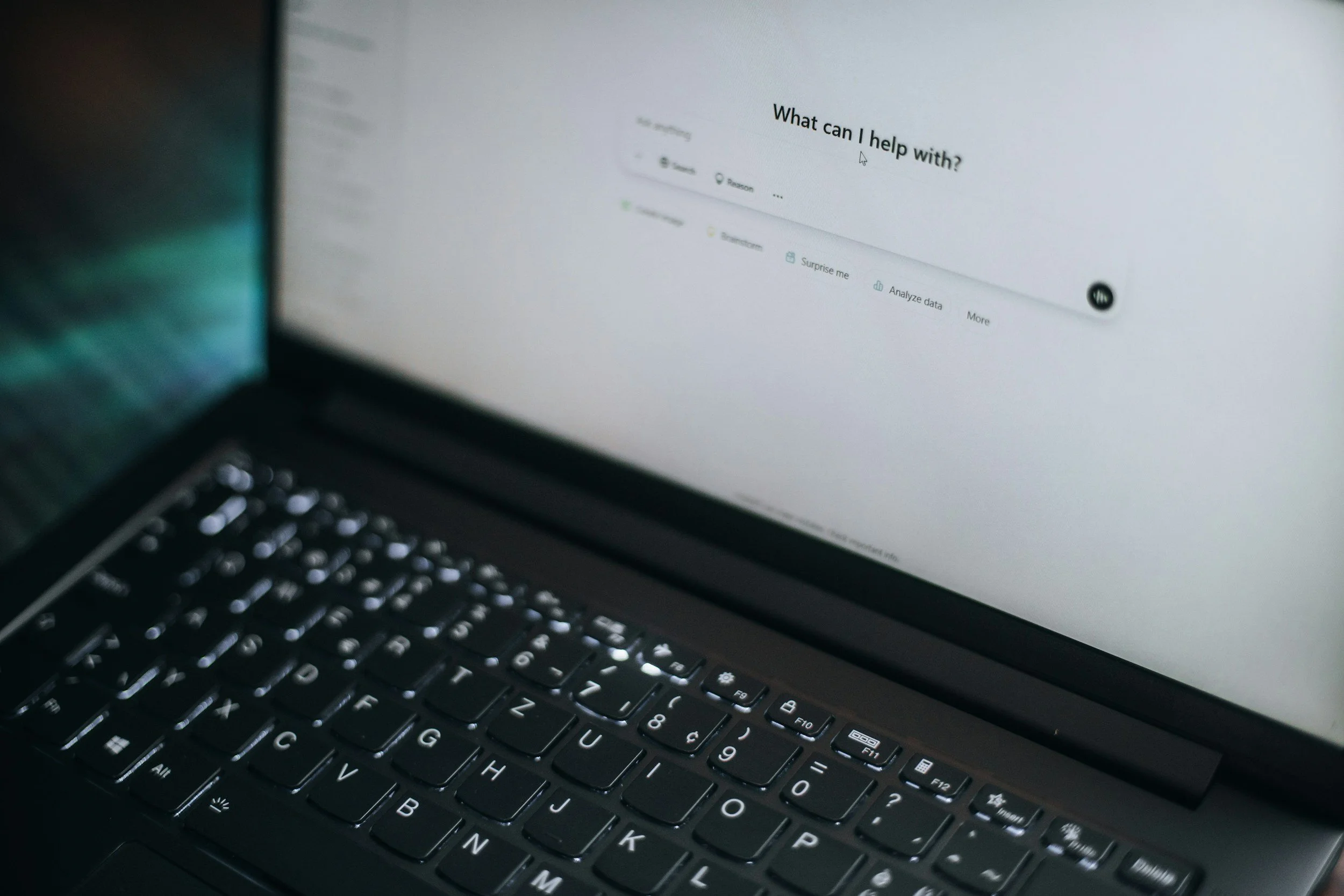A close-up of a laptop showing an AI-driven search interface with the prompt “What can I help with?” — representing the new standard of AI-first content visibility in 2026.