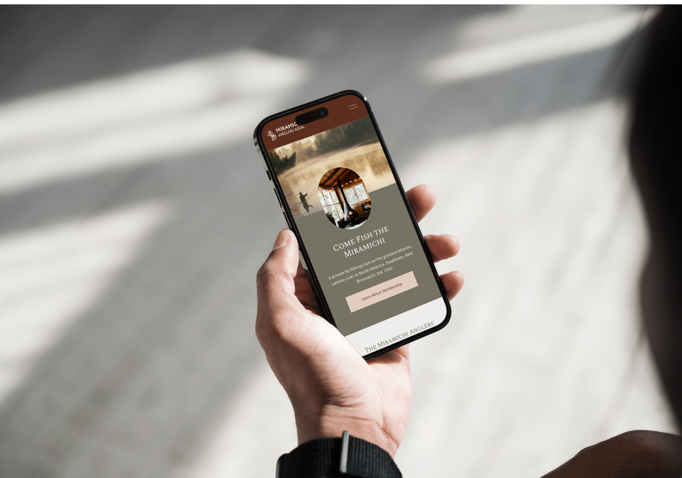 Responsive mobile website design for a fly fishing club displayed on a smartphone in natural outdoor lighting