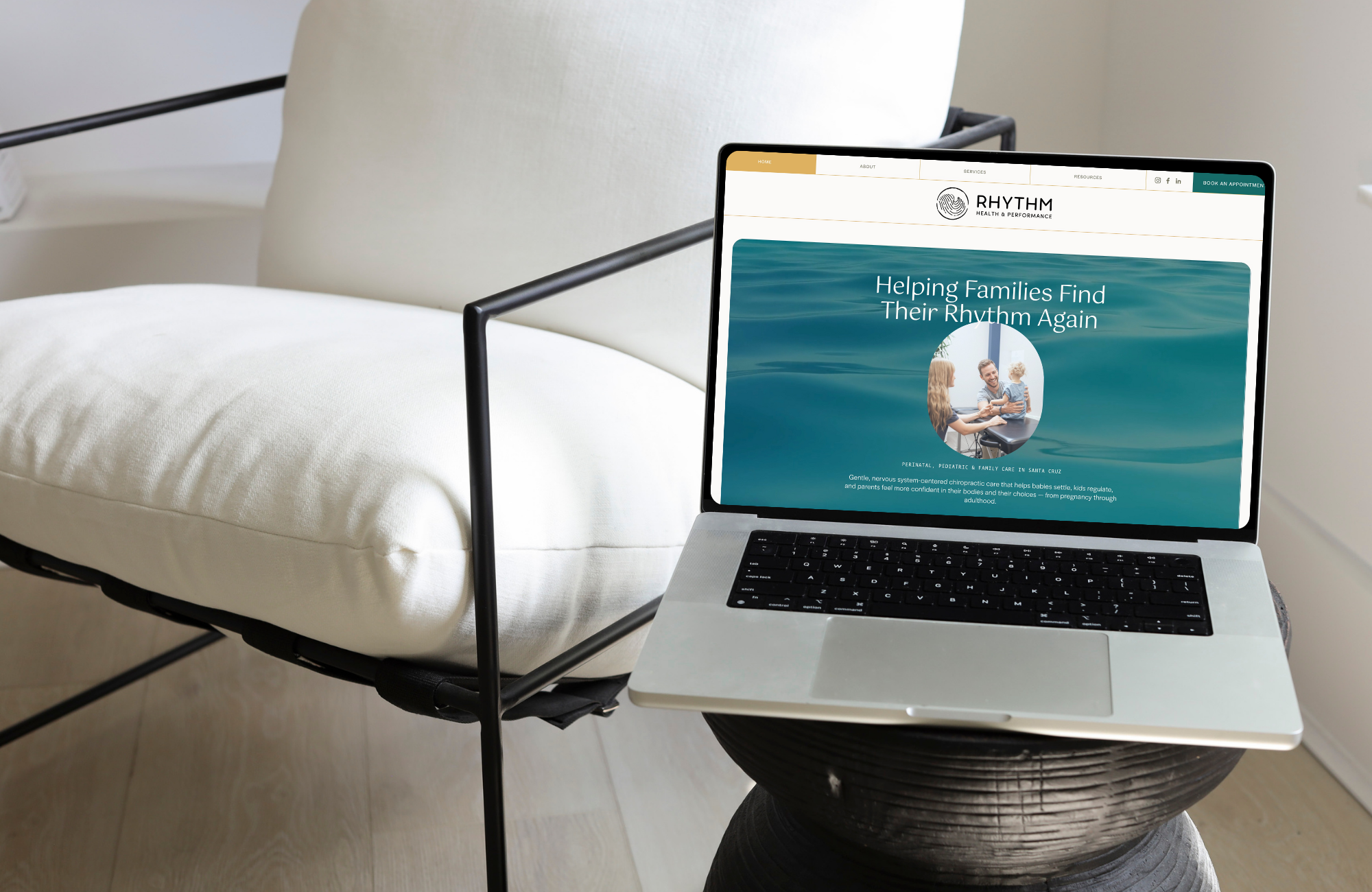 Laptop displaying a website titled 'Helping Families Find Their Rhythm Again' on a nightstand next to a bed with white sheets.