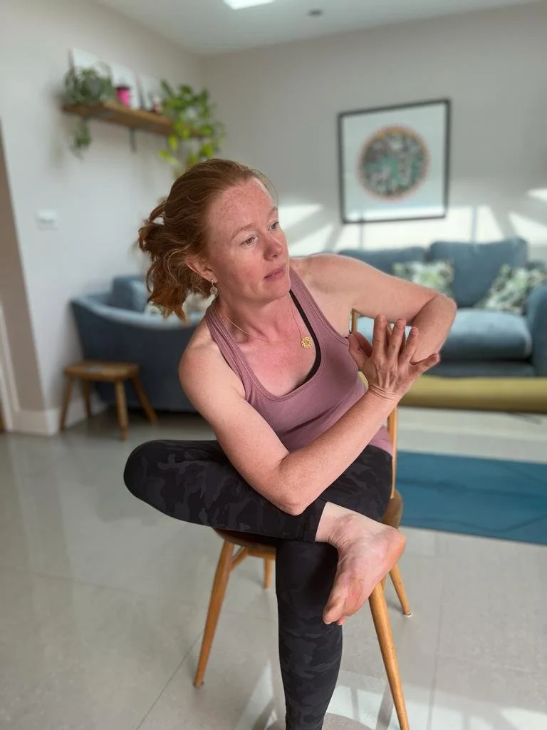 Sophie practicing chair yoga, in pigeon or thread the needle pose, with hands together in front of the chest