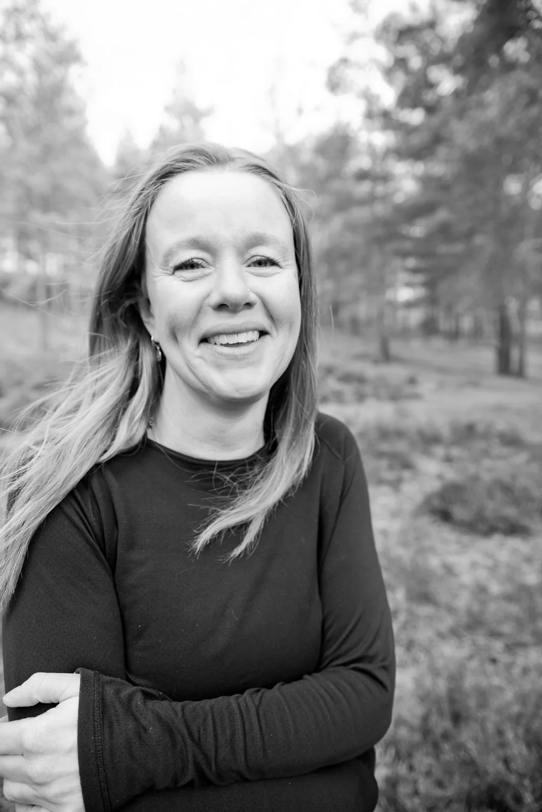 Sophie smiling with long hair standing outdoors in a park with trees.