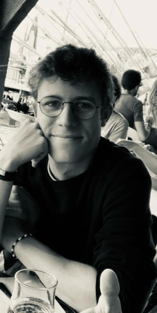 Portrait in black and white of young man with glasses sitting at the a cafe.