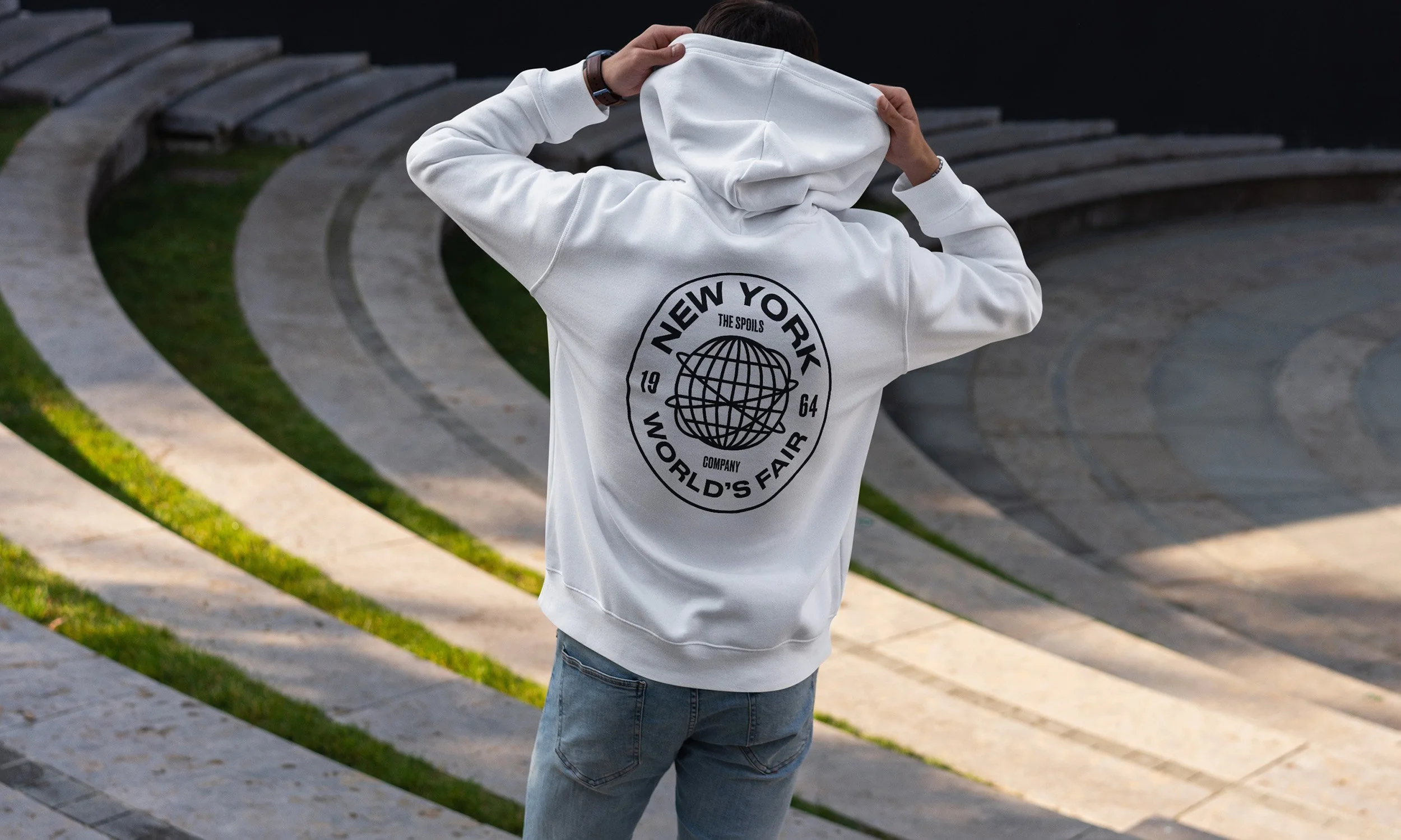 Person wearing a white hoodie with 'New York World's Fair 1964' logo on back, standing outdoors on stone steps.