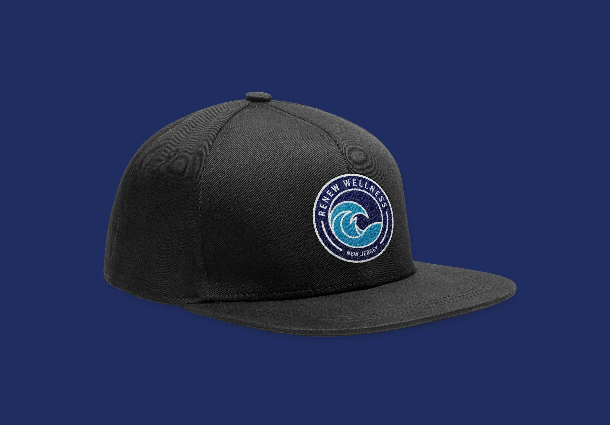 Black baseball cap with a circular patch that says 'Renew Wellness, New Jersey' and features a wave graphic, set against a solid dark blue background.