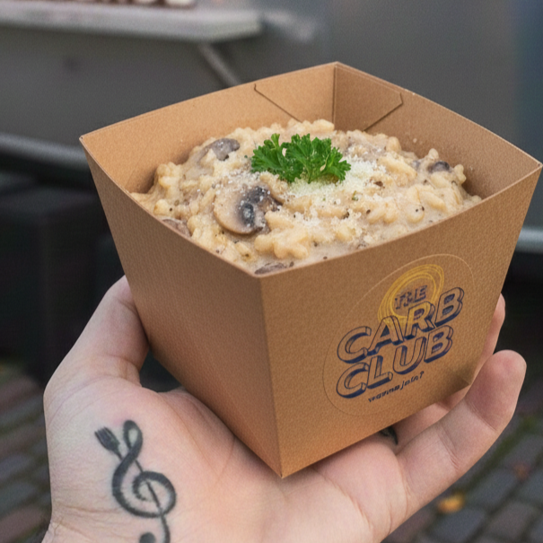 Person holding a cardboard container of macaroni and cheese garnished with parsley, with a band logo that reads "the Carb Club".