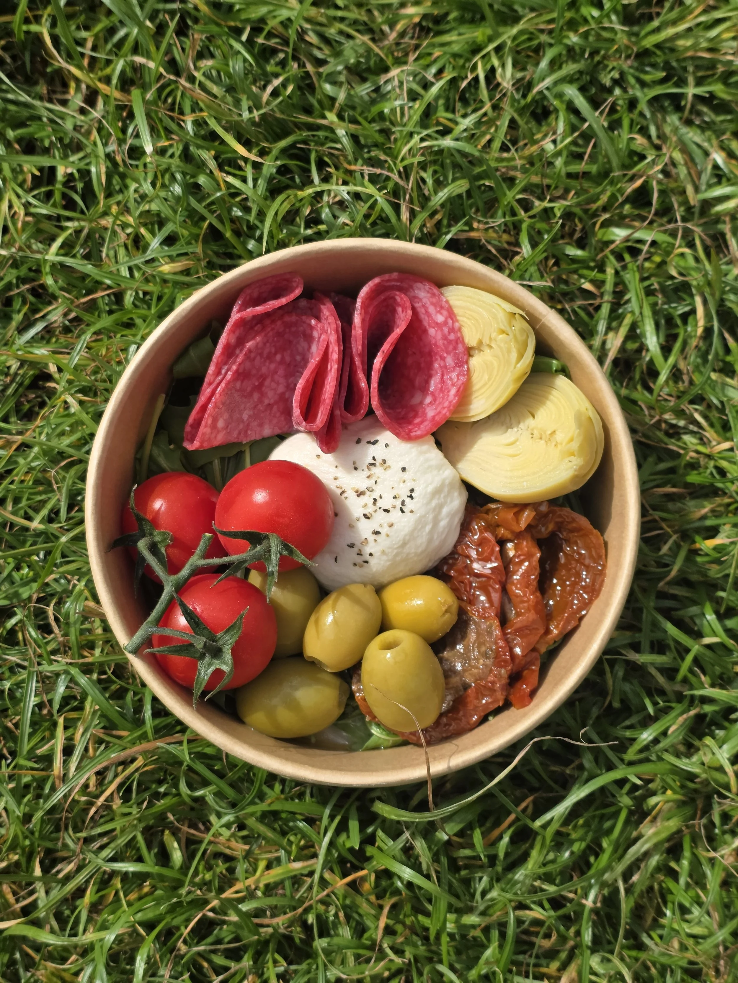 Bowl of pasta topped with cheese, tomato sauce, and herbs, with a label reading 'The Carb Club', outdoors with green grass and blue sky in the background.