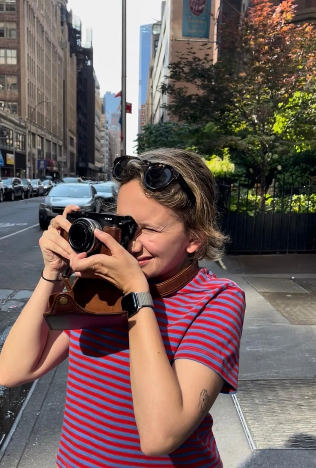 Retrato de fotógrafa trabajando en entorno urbano, capturando una escena en la calle durante un proyecto editorial.