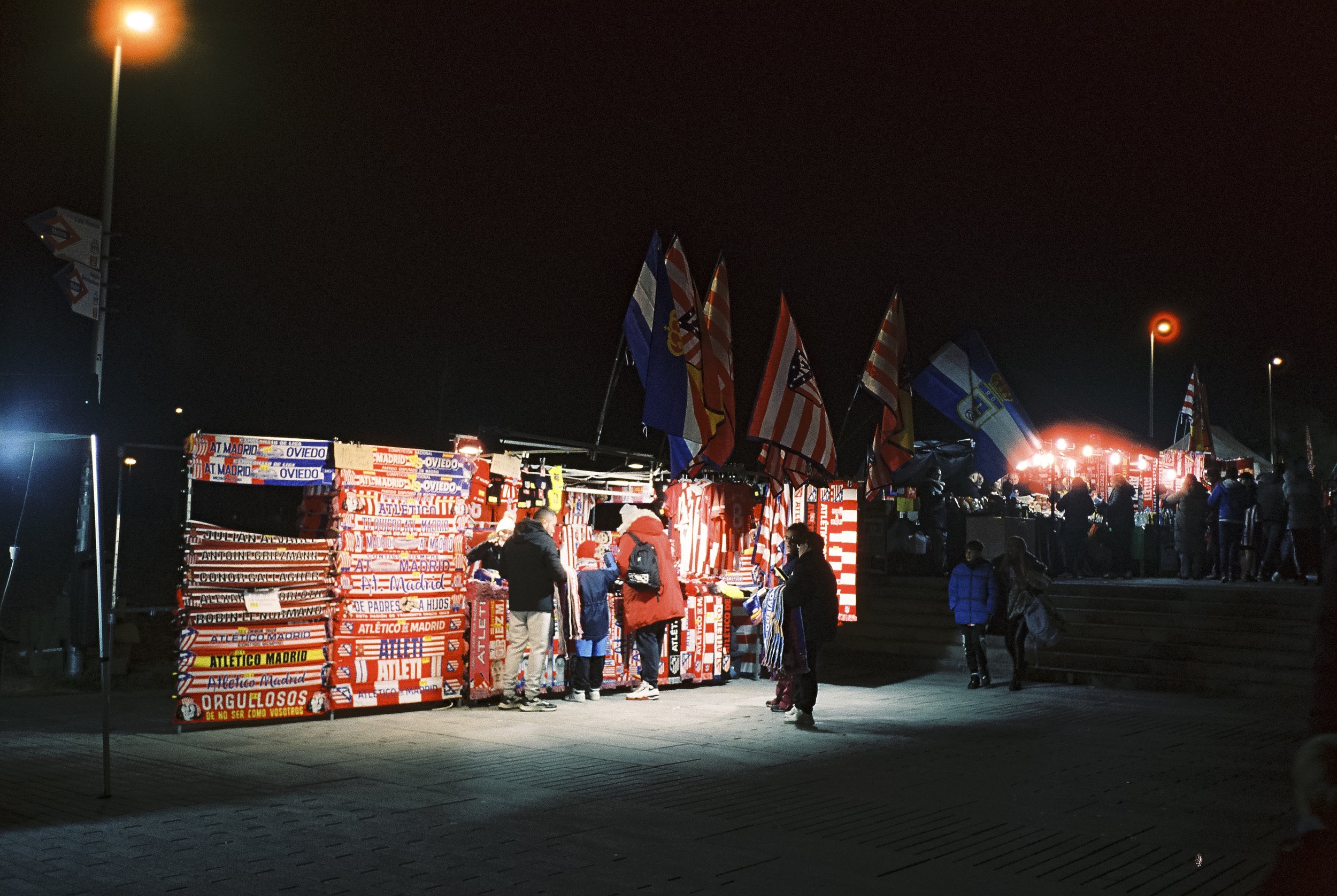 Fotografía analógica realizada en el pre-partido de un encuentro del Atlético de Madrid. Puesto de venta de bufandas como escena cotidiana del entorno futbolístico, capturada en película CineStill 800 desde una mirada documental.