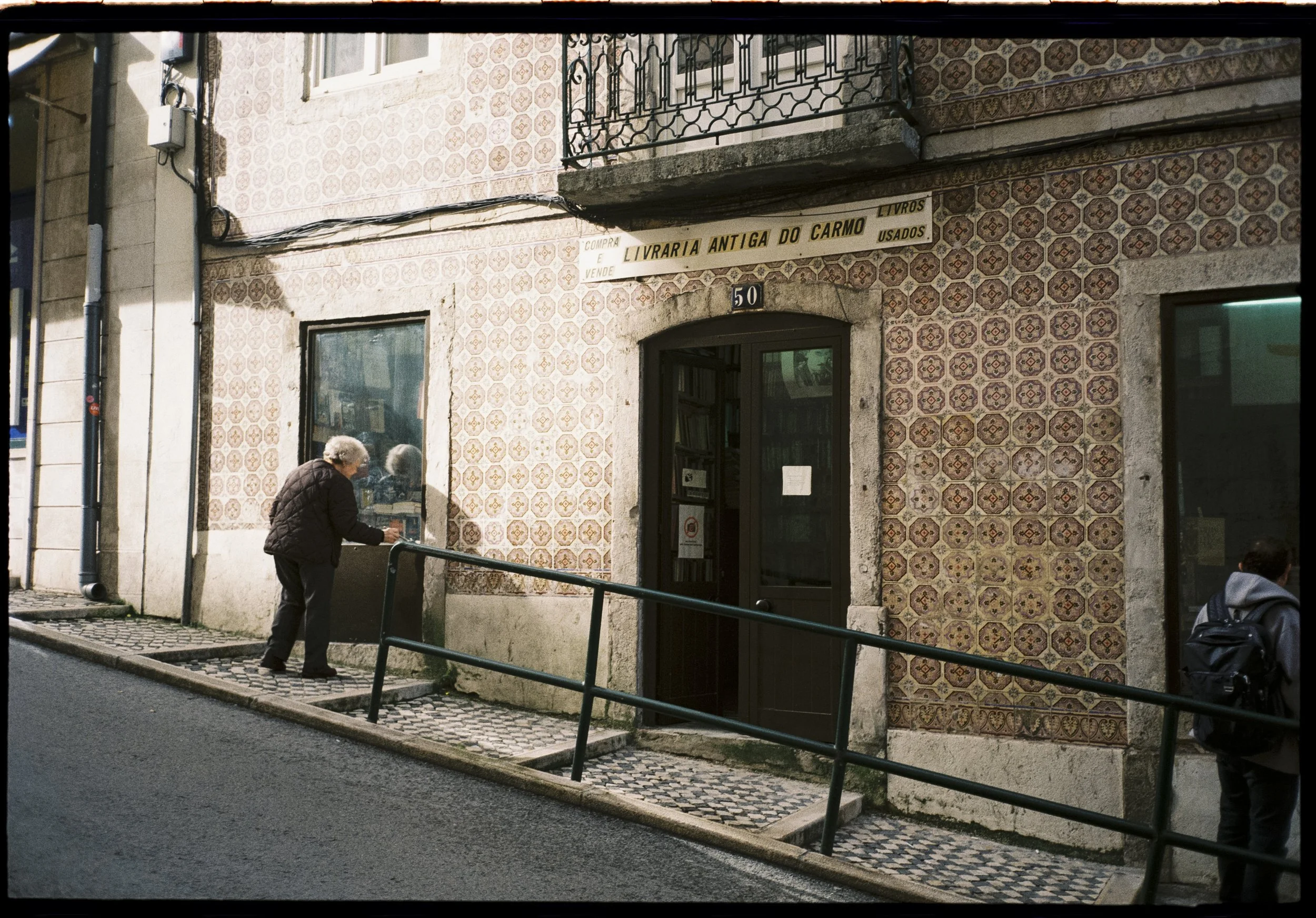 Mujer frente a una librería antigua con fachada de azulejos en Lisboa, fotografía analógica