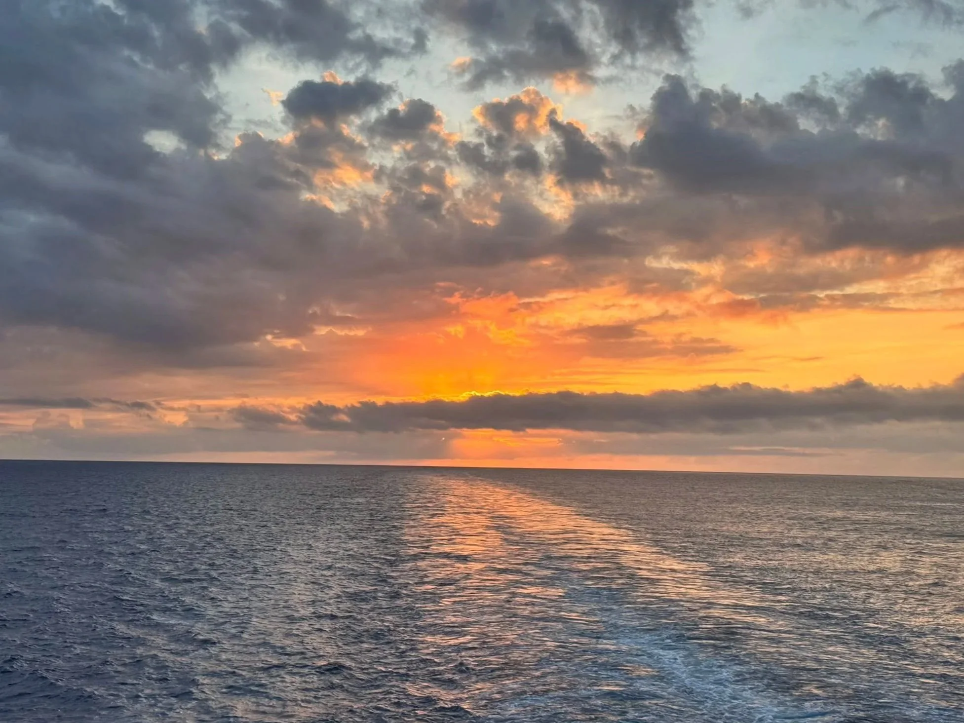 Sunset over the ocean with a partly cloudy sky, orange and yellow hues near the horizon, and gentle waves on the water. nature for mental health, emotional well being, nature walk, forest bathing, exercise, lifestyle modifications, wellness