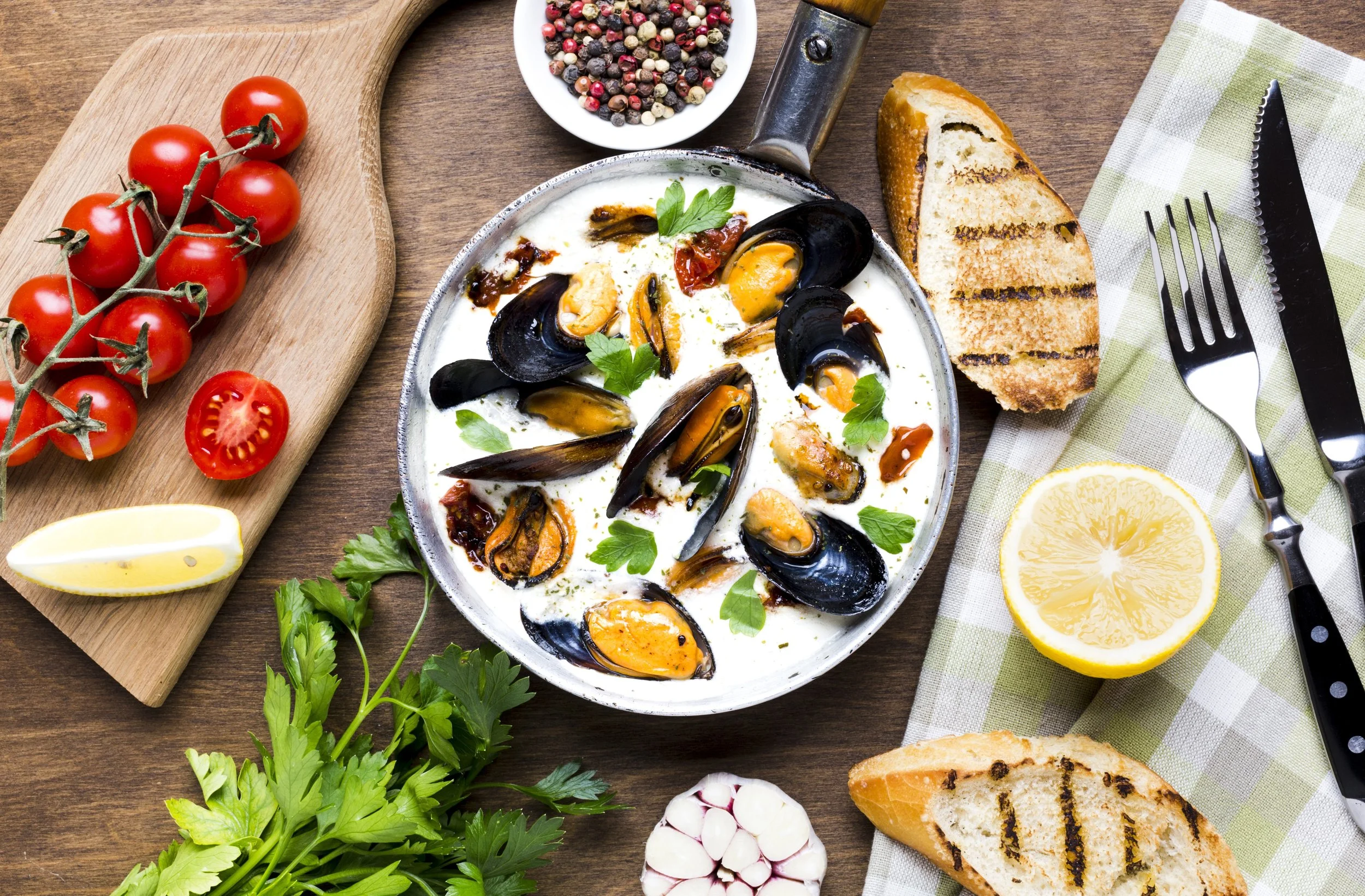 A plate of cooked mussels in a white sauce garnished with parsley, with fresh bread, lemon, cherry tomatoes, garlic, and herbs arranged around it on a wooden table. nature for mental health, emotional well being, nature walk, forest bathing, exercise