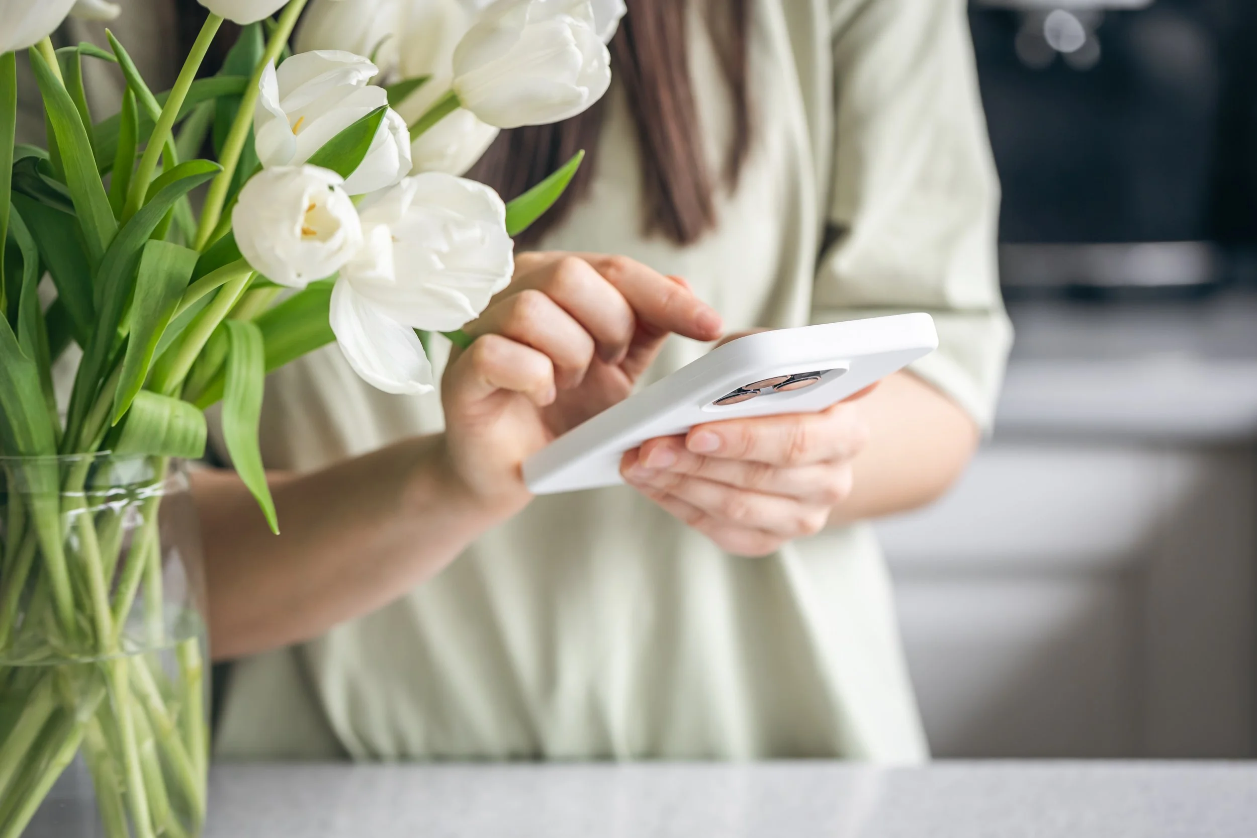 A woman holding a bouquet of white tulips in one hand and using a smartphone with the other hand.
