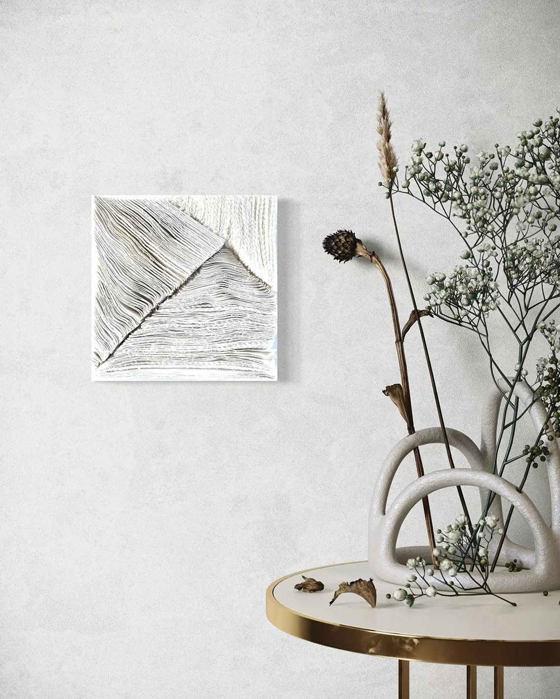 Een witte vaas met decoratieve takken en bloemen op een ronde tafel met een gouden rand, hangend kunstwerk met textuur op de muur.