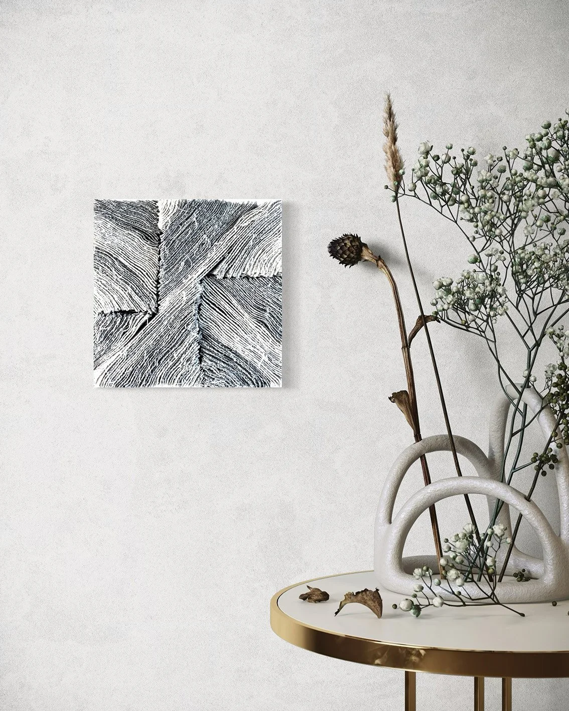 Een wit bloemenvaas met gedroogde takken en kleine witte bloemen, geplaatst op een ronde tafel met gouden rand naast een muur met een zwart-wit kunstwerk.