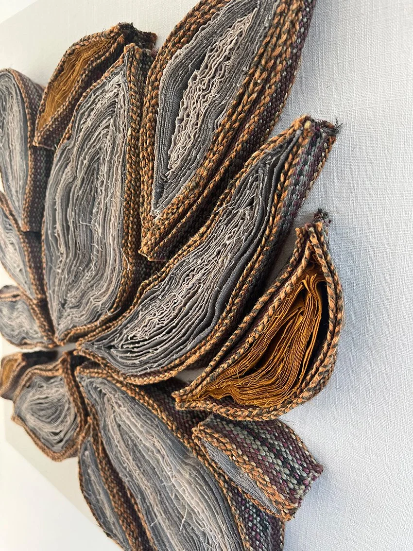 kunstwerk gemaakt van opgerolde en gestapelde oude boekpagina's, gerangschikt in een bloemenpatroon, bevestigd aan een lichte achtergrond.